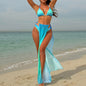 A woman standing on a beach wearing a sky blue bikini top and a matching cover-up skirt in a lighter shade of blue.