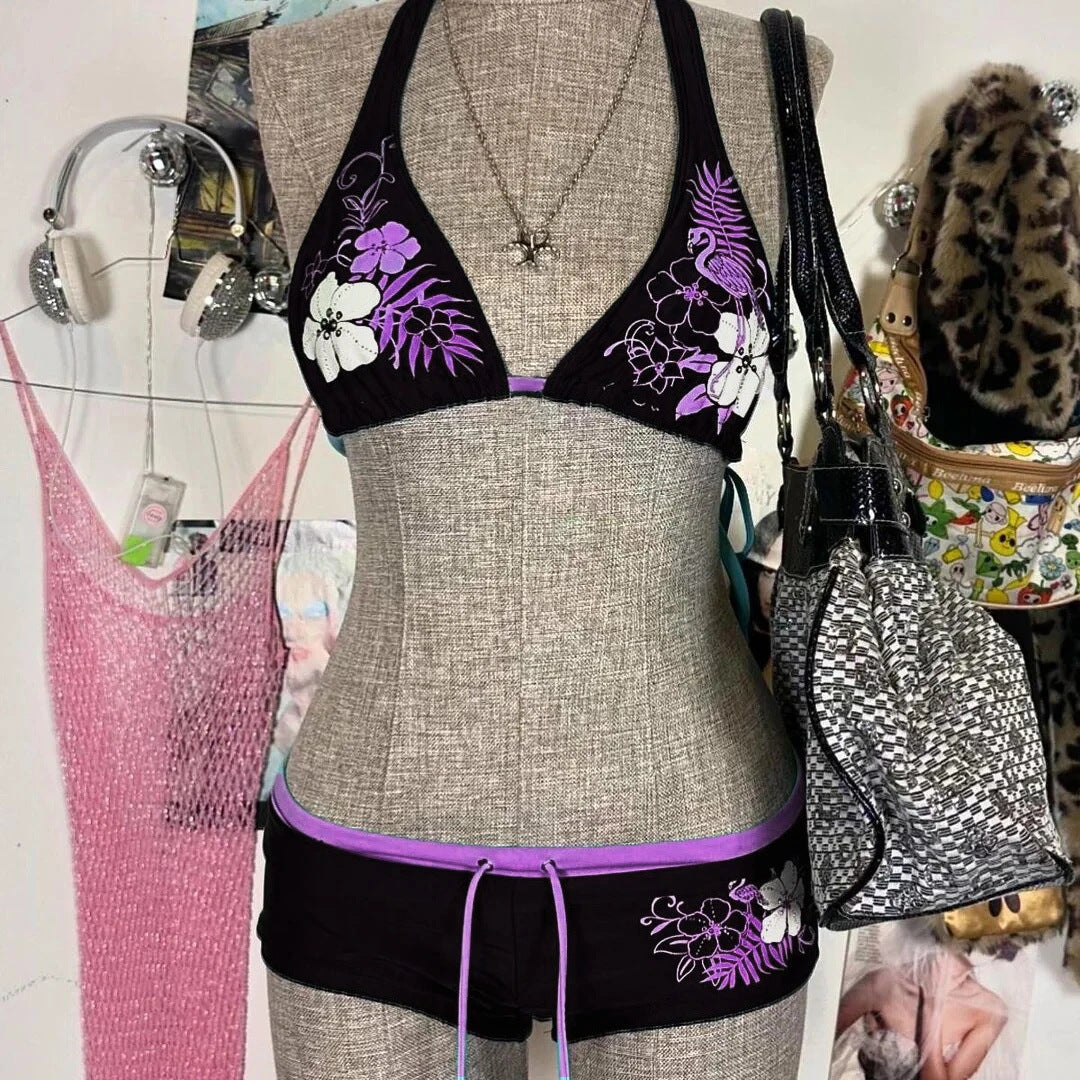 A bikini suit on a mannequin featuring a sky blue top with a floral pattern and a solid black bottom, set against a backdrop with various accessories and clothing items.