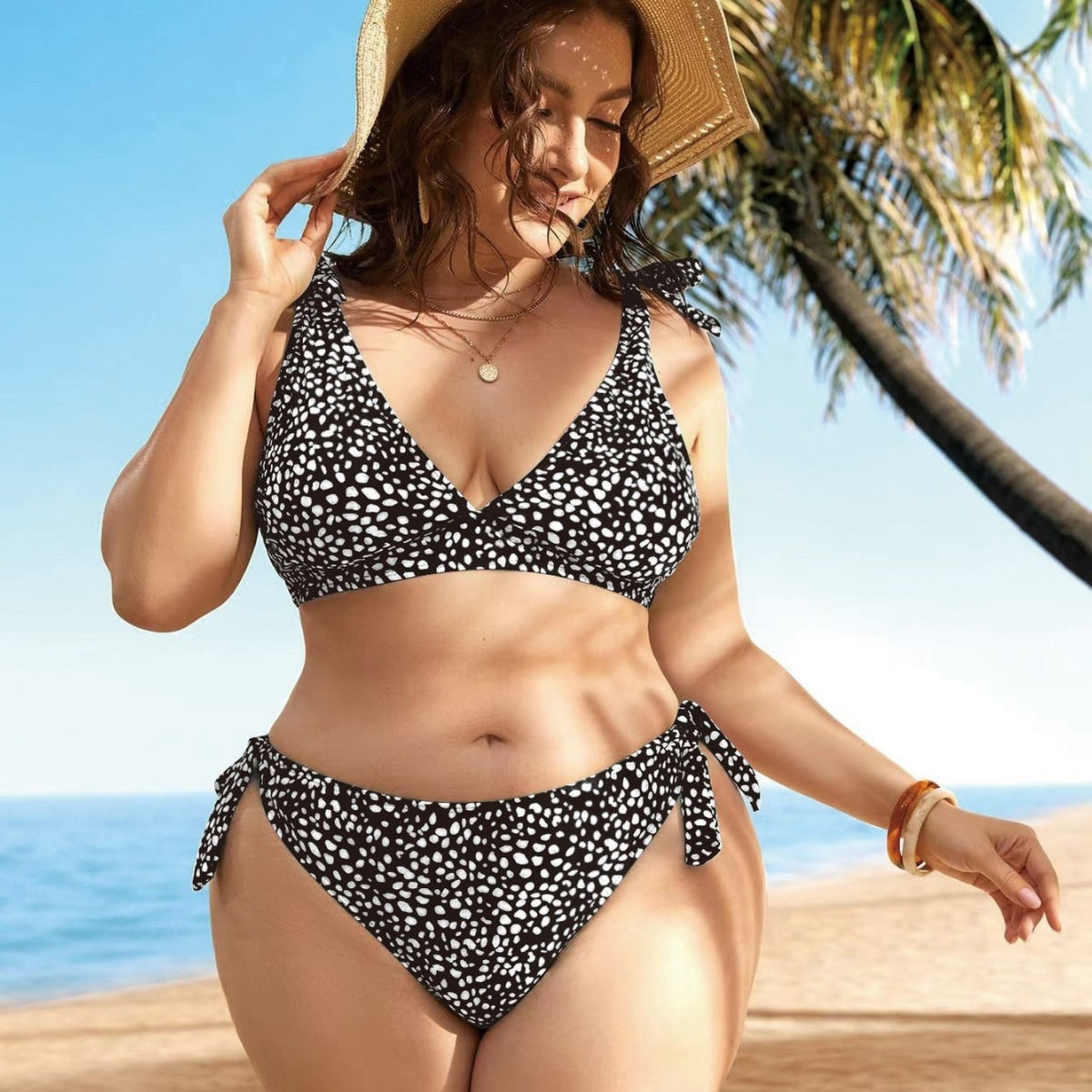 A woman standing on a beach wearing a green bikini with a floral pattern, featuring a V-neck top and tie-side bottoms.