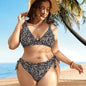 A woman standing on a beach wearing a green bikini with a floral pattern, featuring a V-neck top and tie-side bottoms.