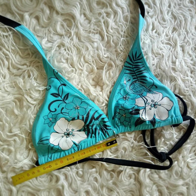 Teal bikini set with floral designs on a textured white background.