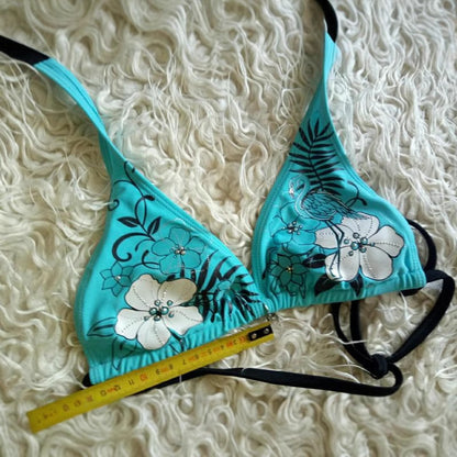 Teal bikini set with floral designs on a textured white background.