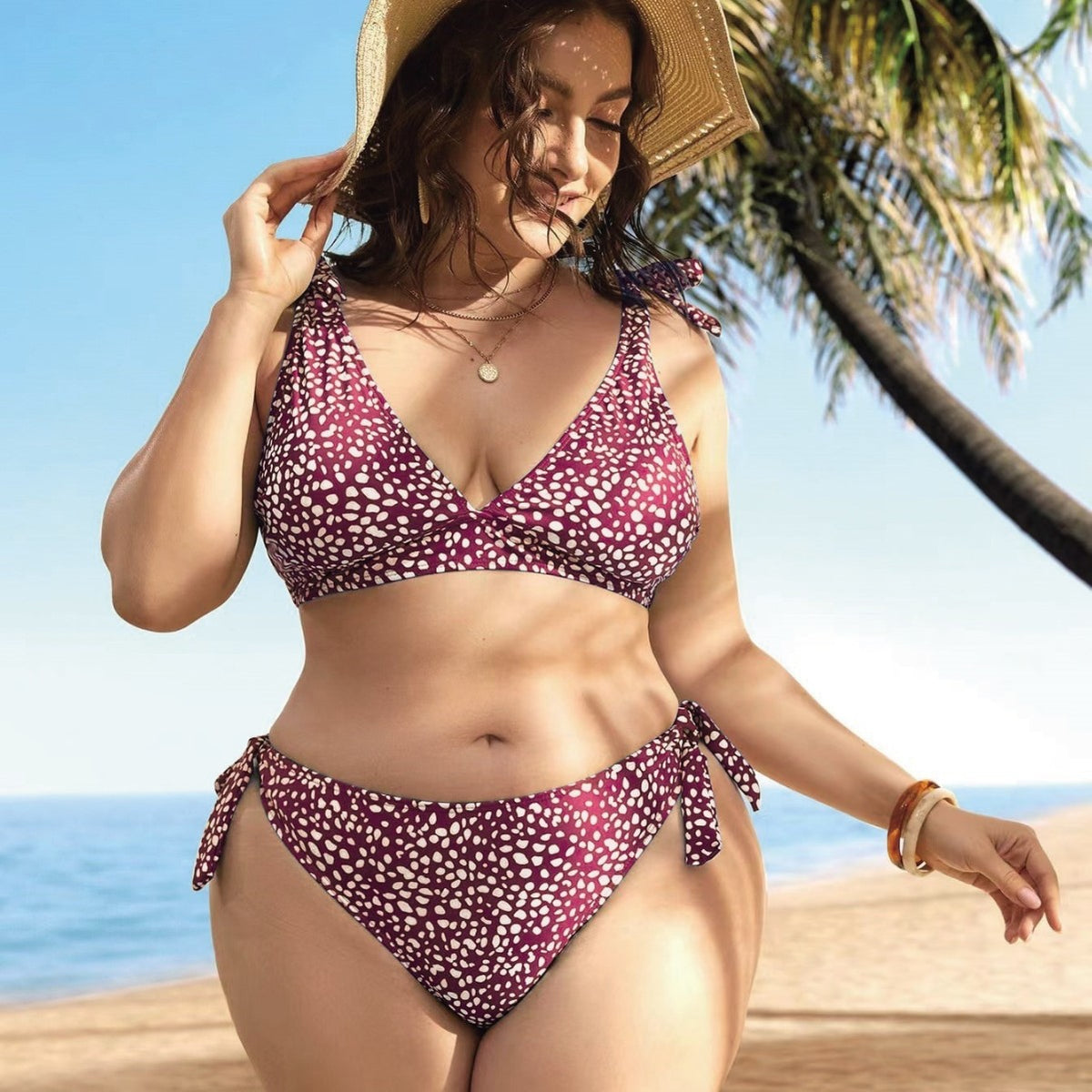 A woman standing on a beach wearing a green bikini with a floral pattern, featuring a V-neck top and tie-side bottoms.
