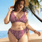 A woman standing on a beach wearing a green bikini with a floral pattern, featuring a V-neck top and tie-side bottoms.