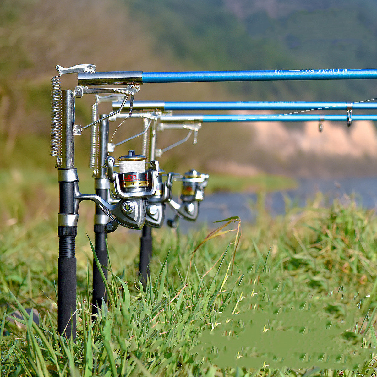 A set of surf fishing rods with reels and automatic sea fishing rod accessories, placed on a grassy area near a body of water.