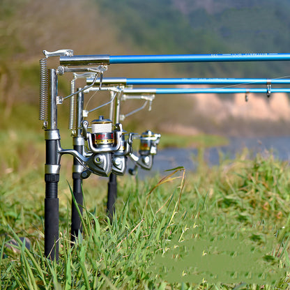 A set of surf fishing rods with reels and automatic sea fishing rod accessories, placed on a grassy area near a body of water.