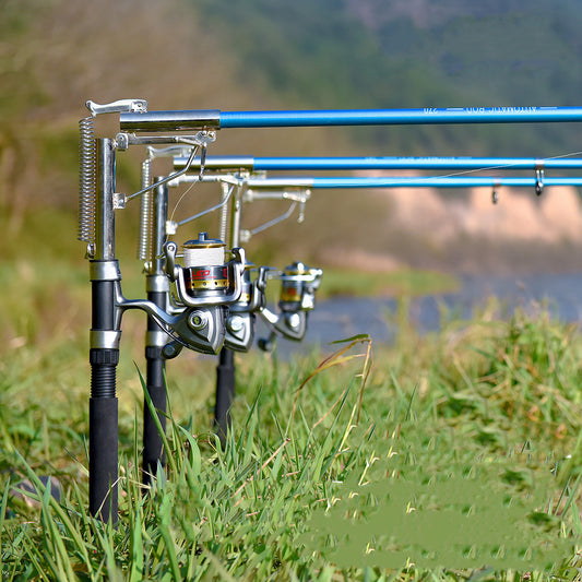 A set of surf fishing rods with reels and automatic sea fishing rod accessories, placed on a grassy area near a body of water.