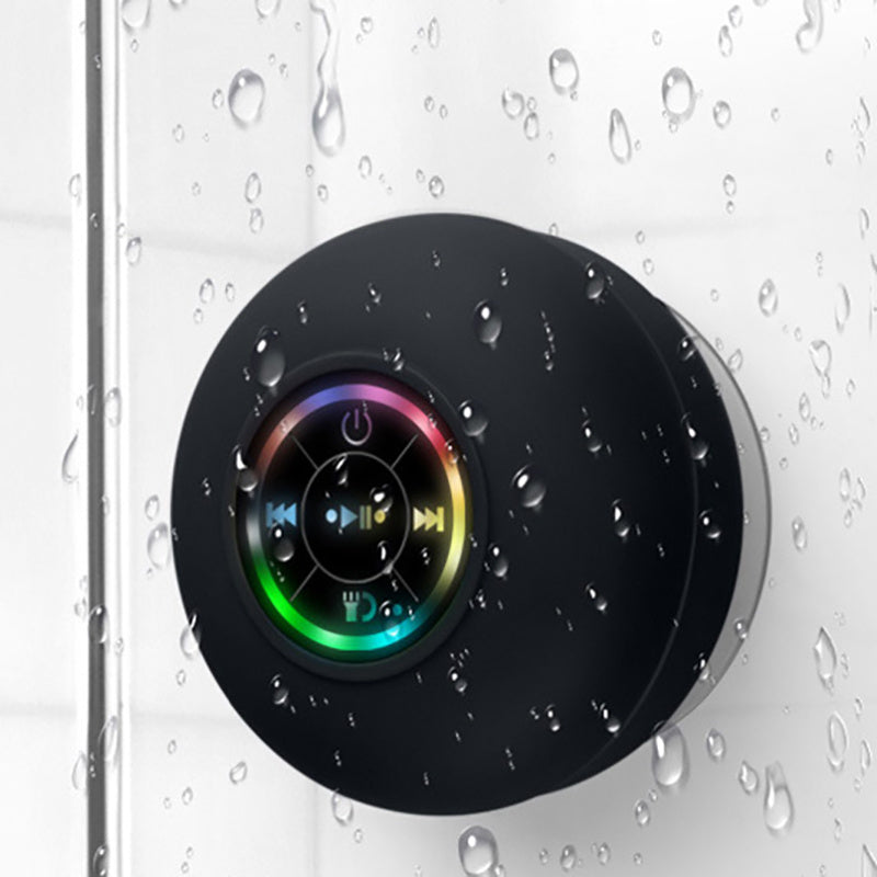 A black waterproof Bluetooth speaker with LED light strips attached to a tiled wall, presumably in a shower setting.
