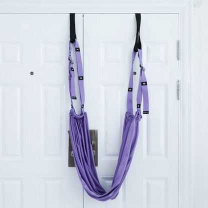 A person using a purple yoga inversion and stretching strap to assist with a yoga pose, hanging from a door frame.
