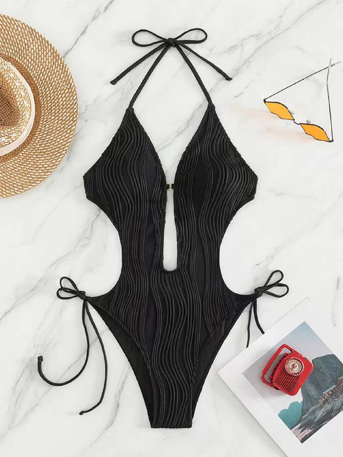 Black ribbed swimsuit on a marble surface with accessories.