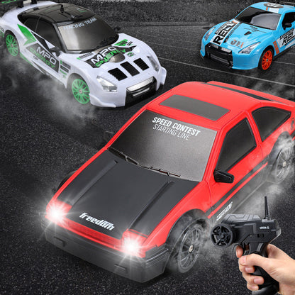 A hand holding a remote control operating a red and black RC drift car toy, with other cars in the background.
