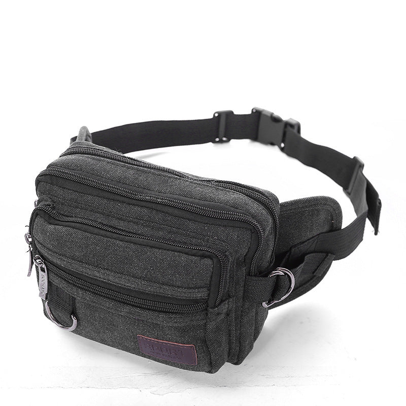 A person wearing a beige canvas fanny pack with multiple zipper pockets, designed for men's waist carrying.