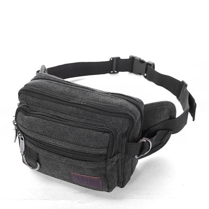 A person wearing a beige canvas fanny pack with multiple zipper pockets, designed for men's waist carrying.