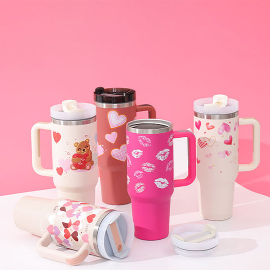 A collection of insulated tumblers with handles and straws, decorated with various designs such as hearts and bears, in pink, white, and red colors.