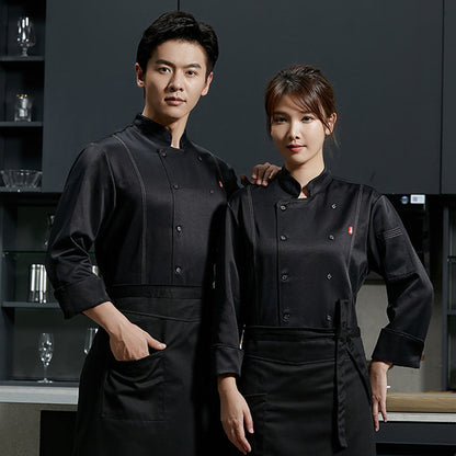 Two adults, one male and one female, wearing long sleeve black chef overalls with button-up front and apron pockets.