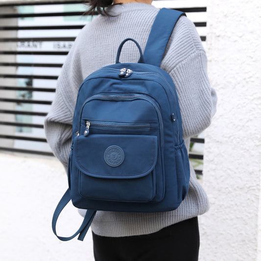 A person wearing a gray sweater carrying a dark blue backpack with multiple compartments and a front logo.