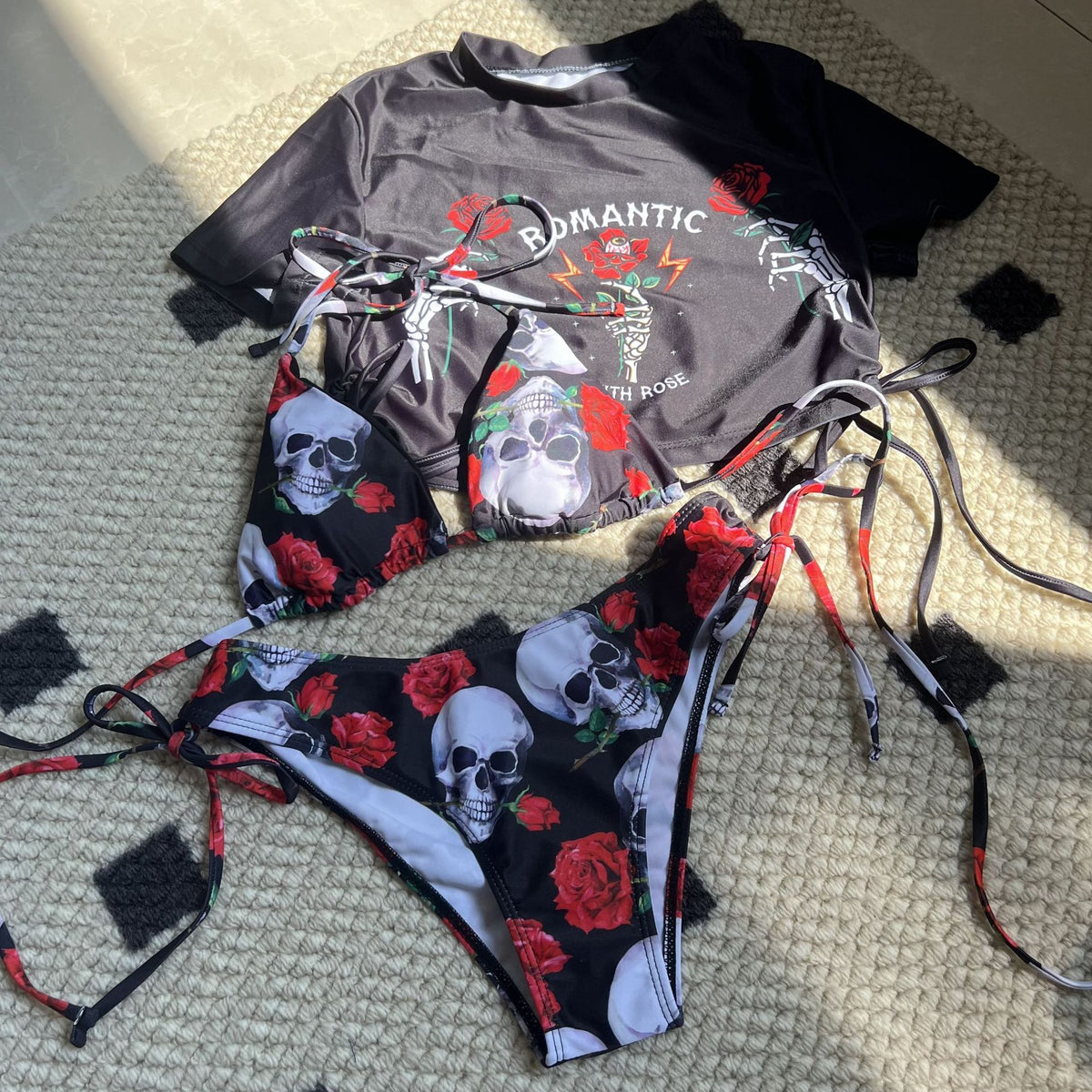 Bikini set with skull and rose design laid on a textured surface.