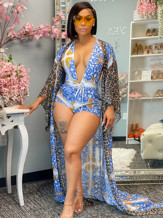 A model wearing a three-piece shawl bikini shorts swimsuit in a blue floral pattern with a leopard print shawl.